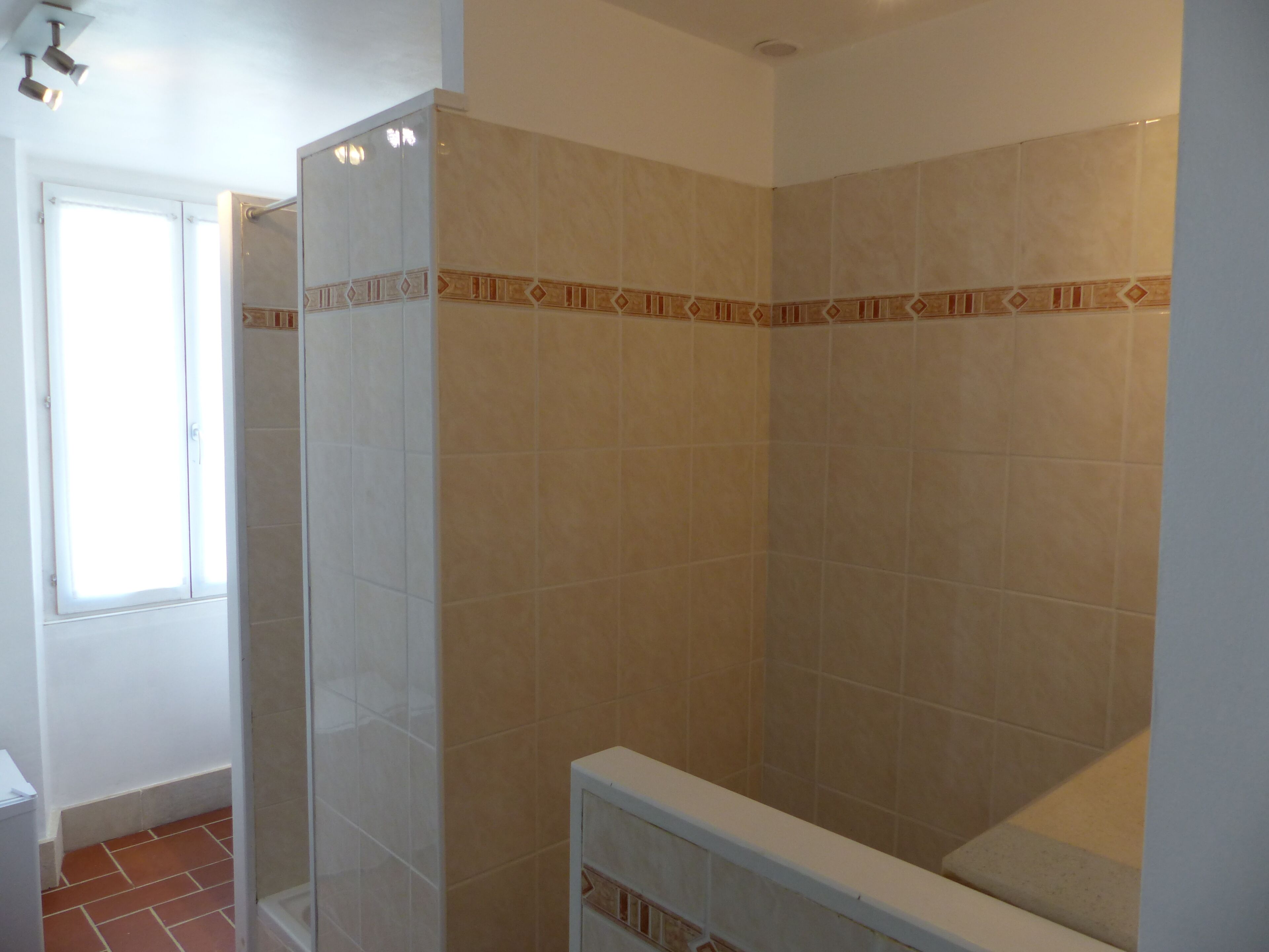A bathroom with beige tiles, a shower, and a window.