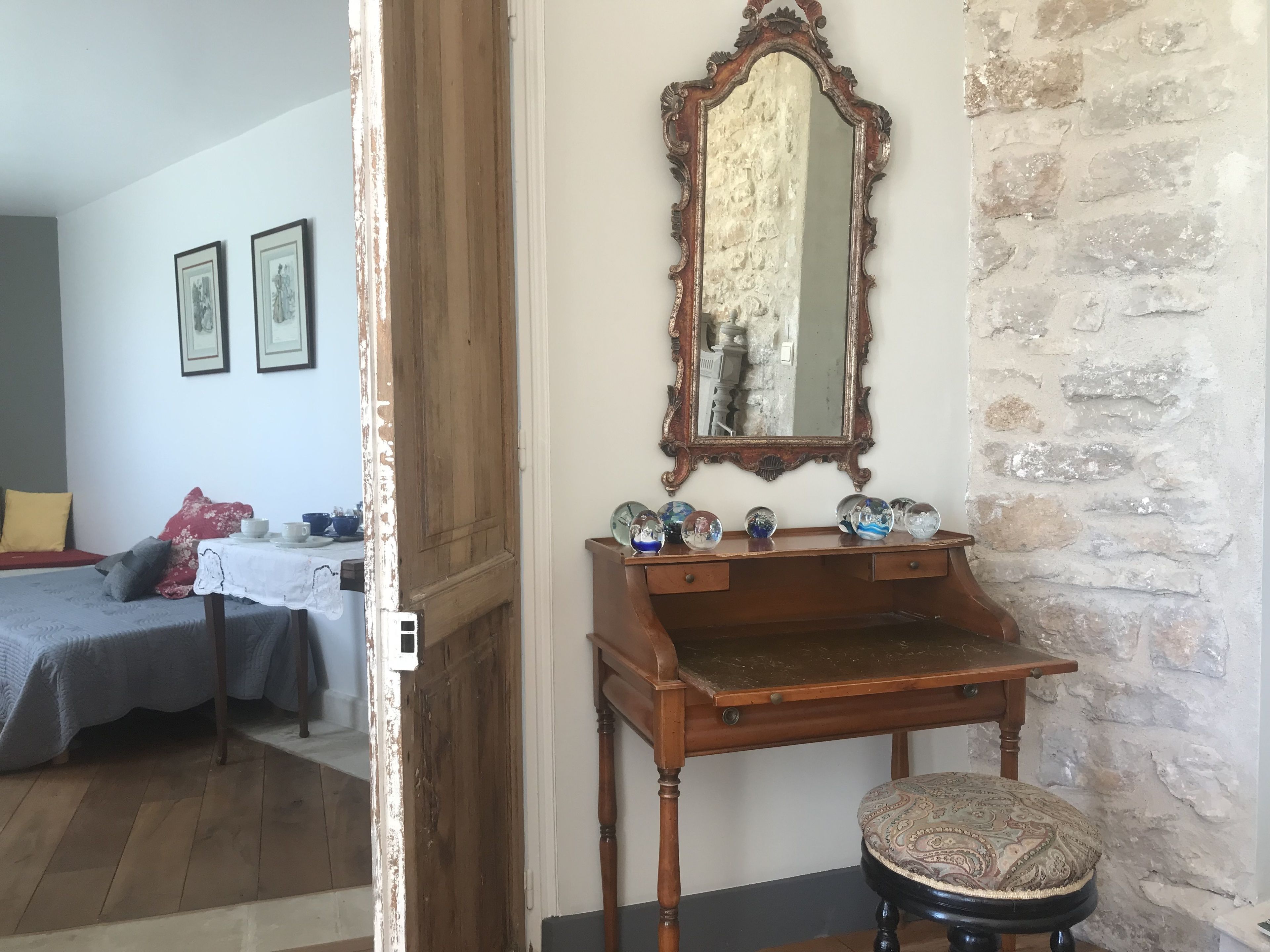 Une chambre avec une commode en bois, un miroir et un lit recouvert d’une couverture rouge et grise.