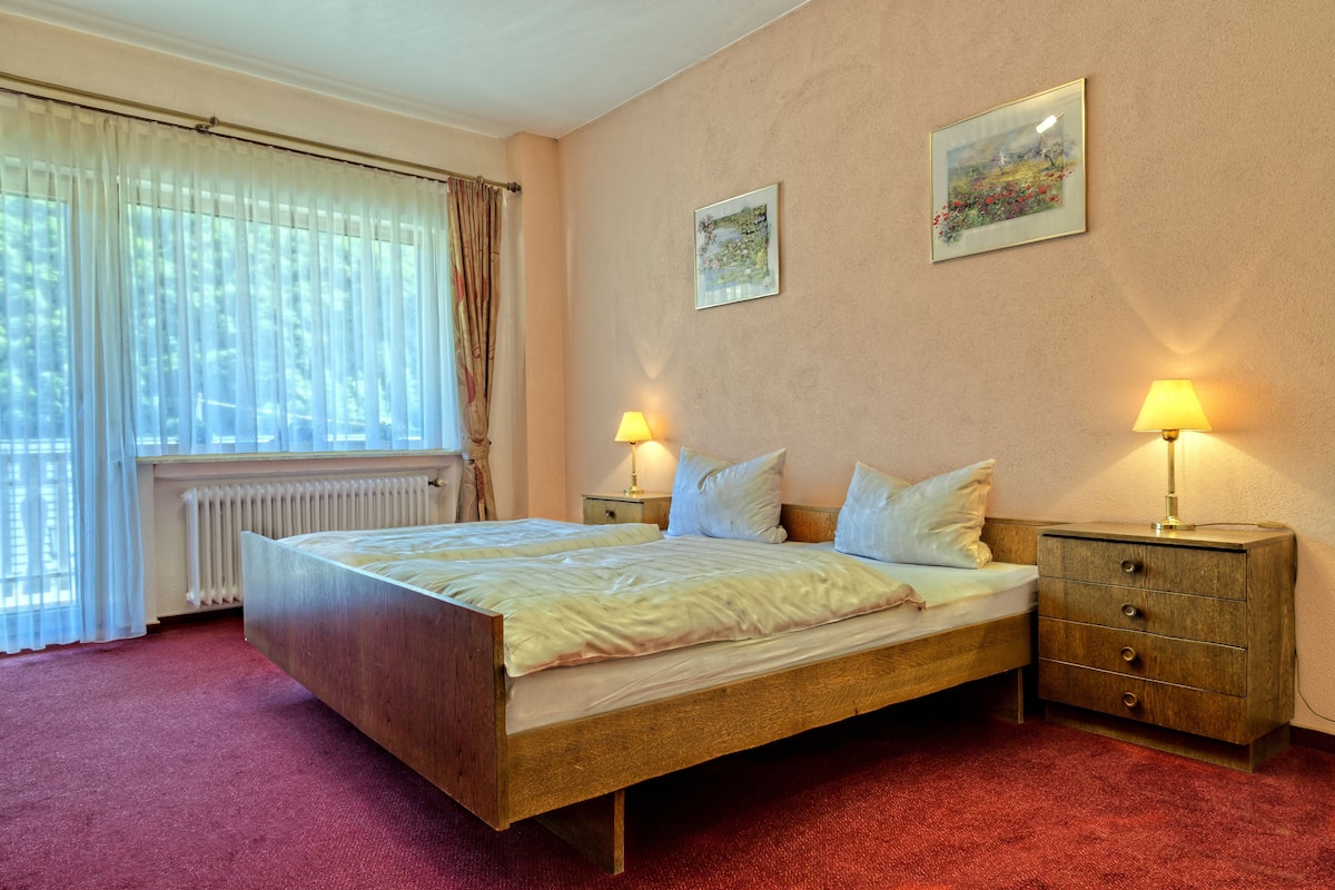 A bedroom with a wooden bed, two bedside tables with lamps, a radiator, and two framed pictures on the wall.