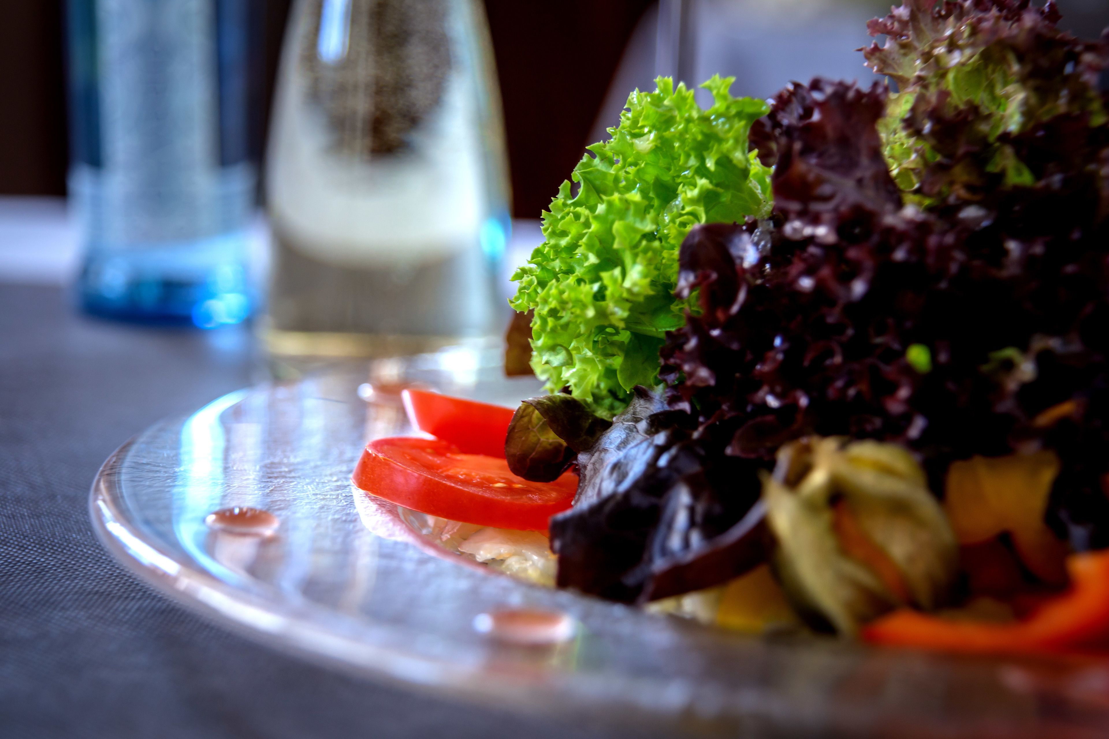 A clear glass plate with a salad consisting of lettuce, tomato slices, and capers.