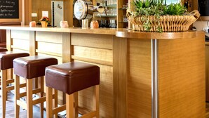 A bar area with wooden stools, a bar counter, and a sign that reads "Welcome". - Hotel zur Brücke (Minheim)