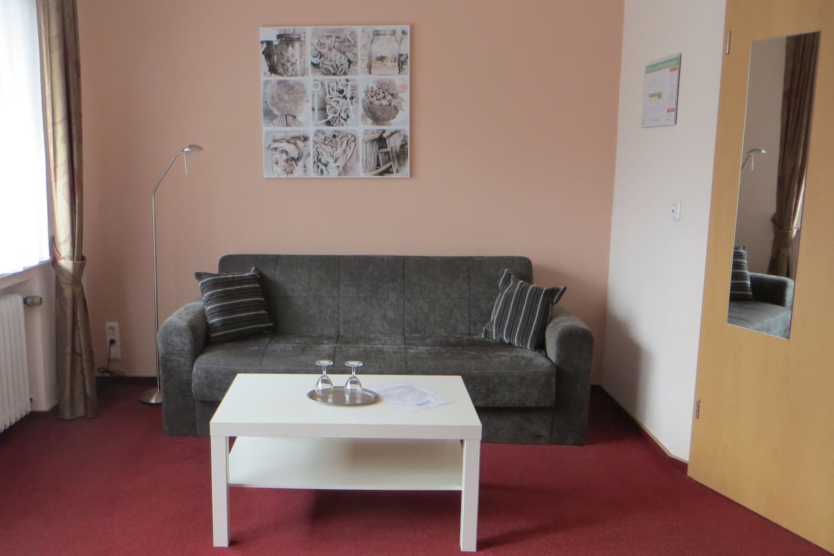 A room with a grey sofa, a white table with two wine glasses, a radiator, and a wall with a collage of photos.