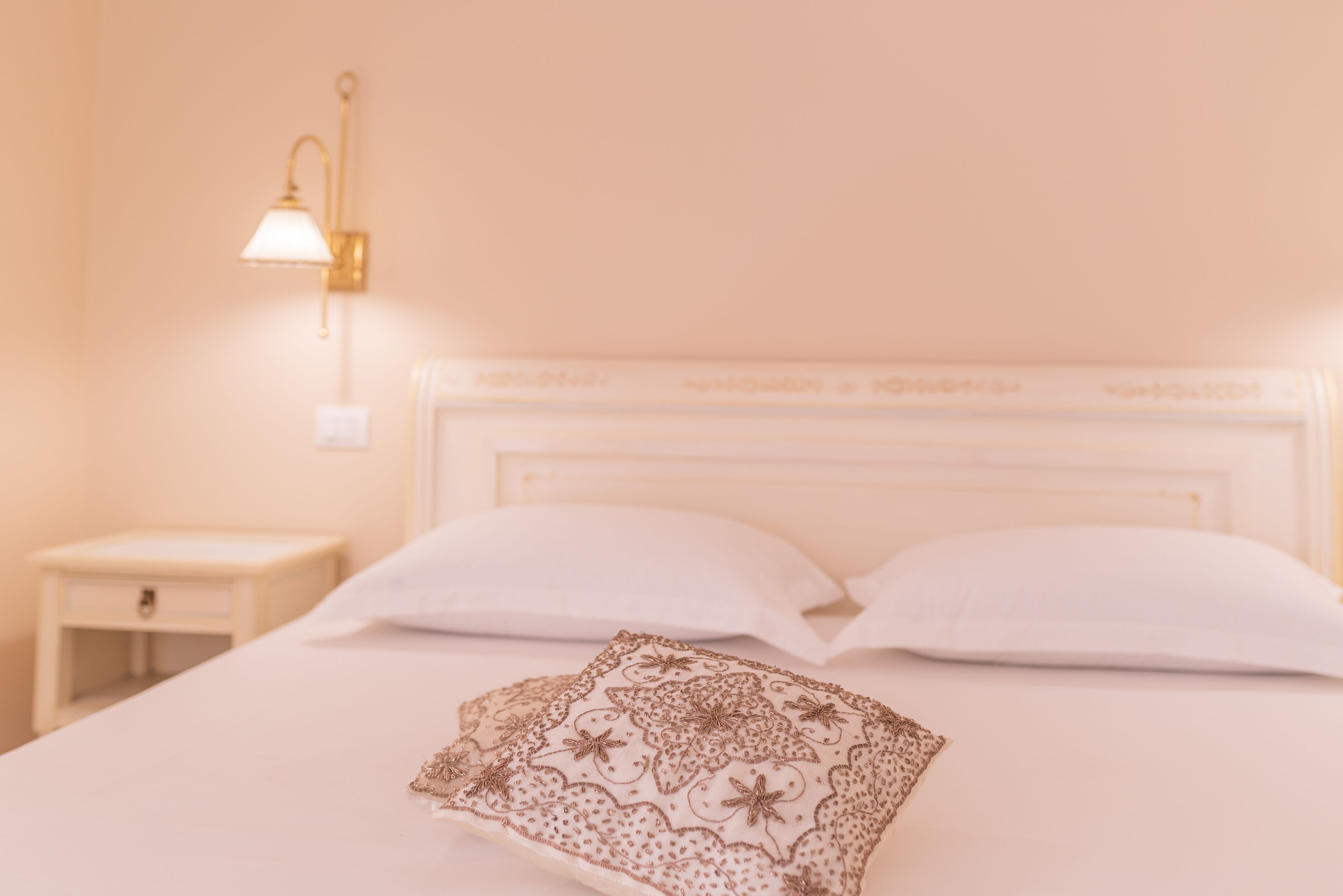 A neatly made bed with a white headboard, a bedside table, and a wall-mounted lamp.