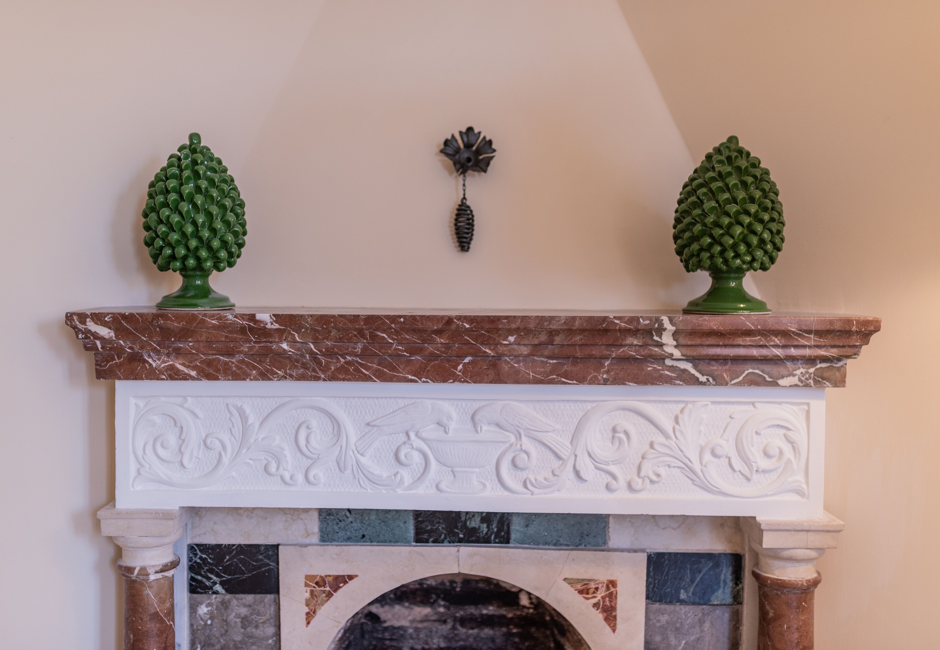 A fireplace with a marble mantel and two green pinecone-shaped decorations on top.