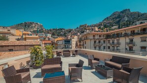 Una terraza al aire libre con muebles de mimbre y vistas a un pueblo en la ladera de una colina.