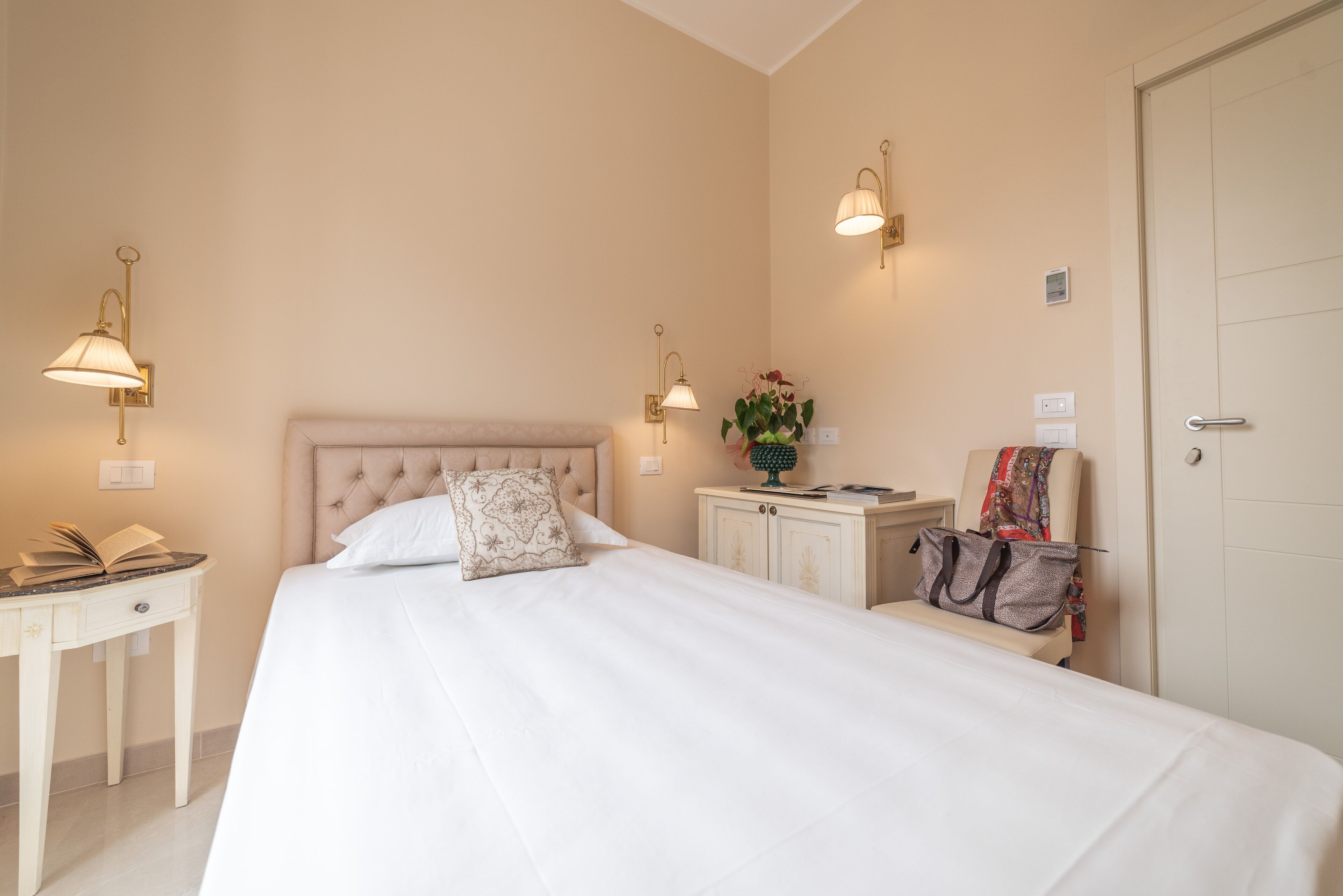 A hotel room with a large bed, bedside tables, a nightstand, a lamp, and a door.
