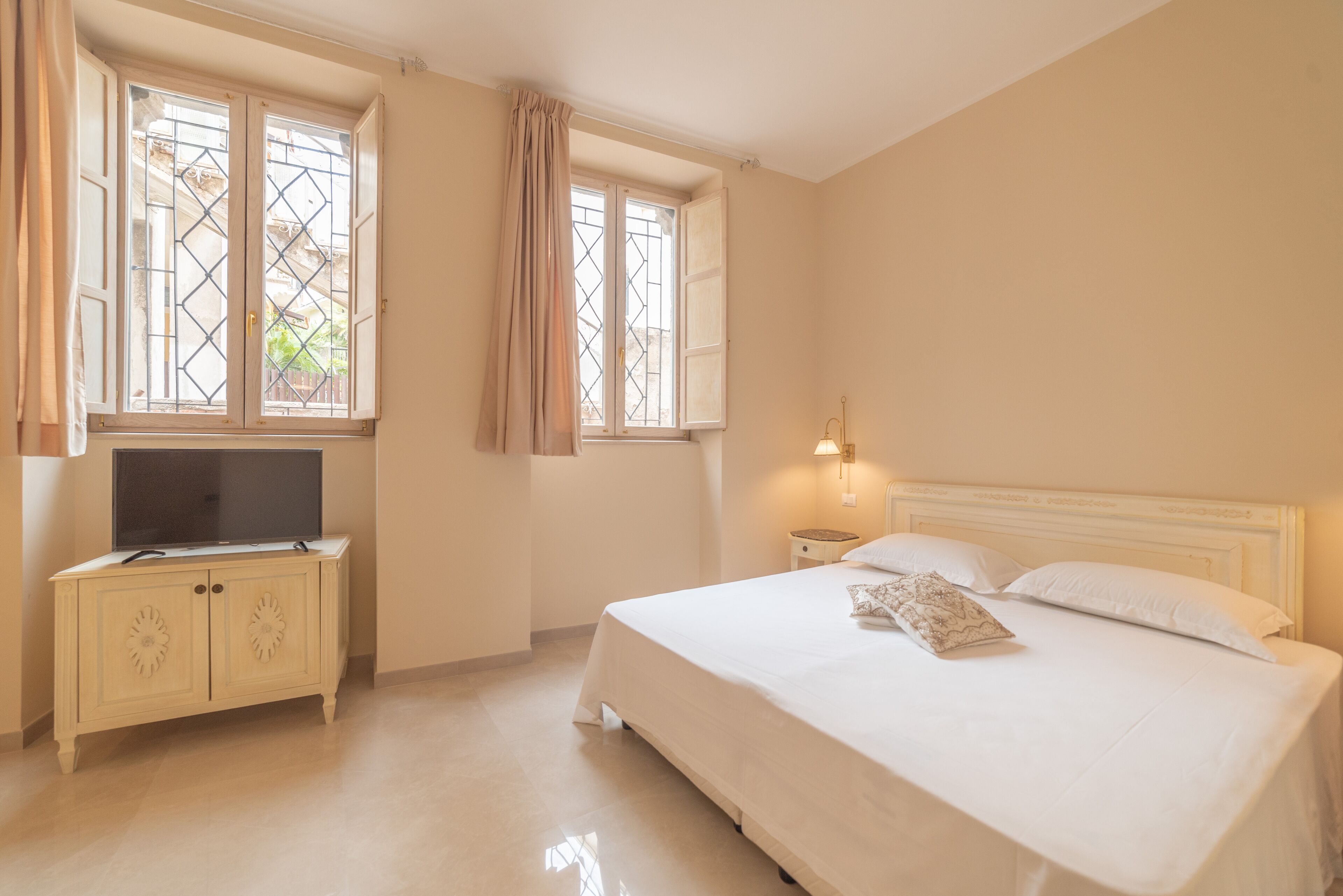 A bedroom with a bed, a TV on a cabinet, and a window with curtains.