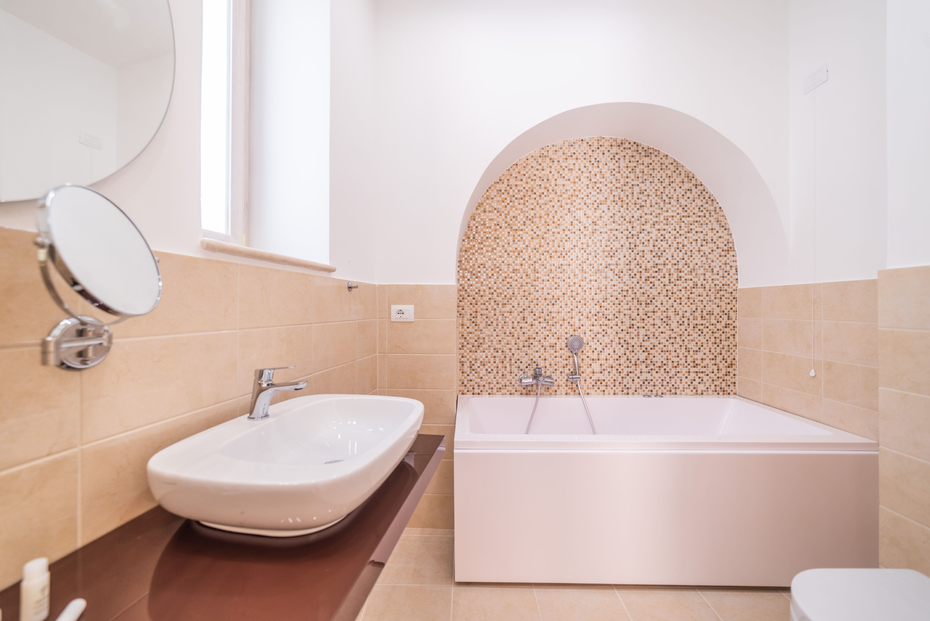 A modern bathroom with a large bathtub, a round mirror, and a sink.