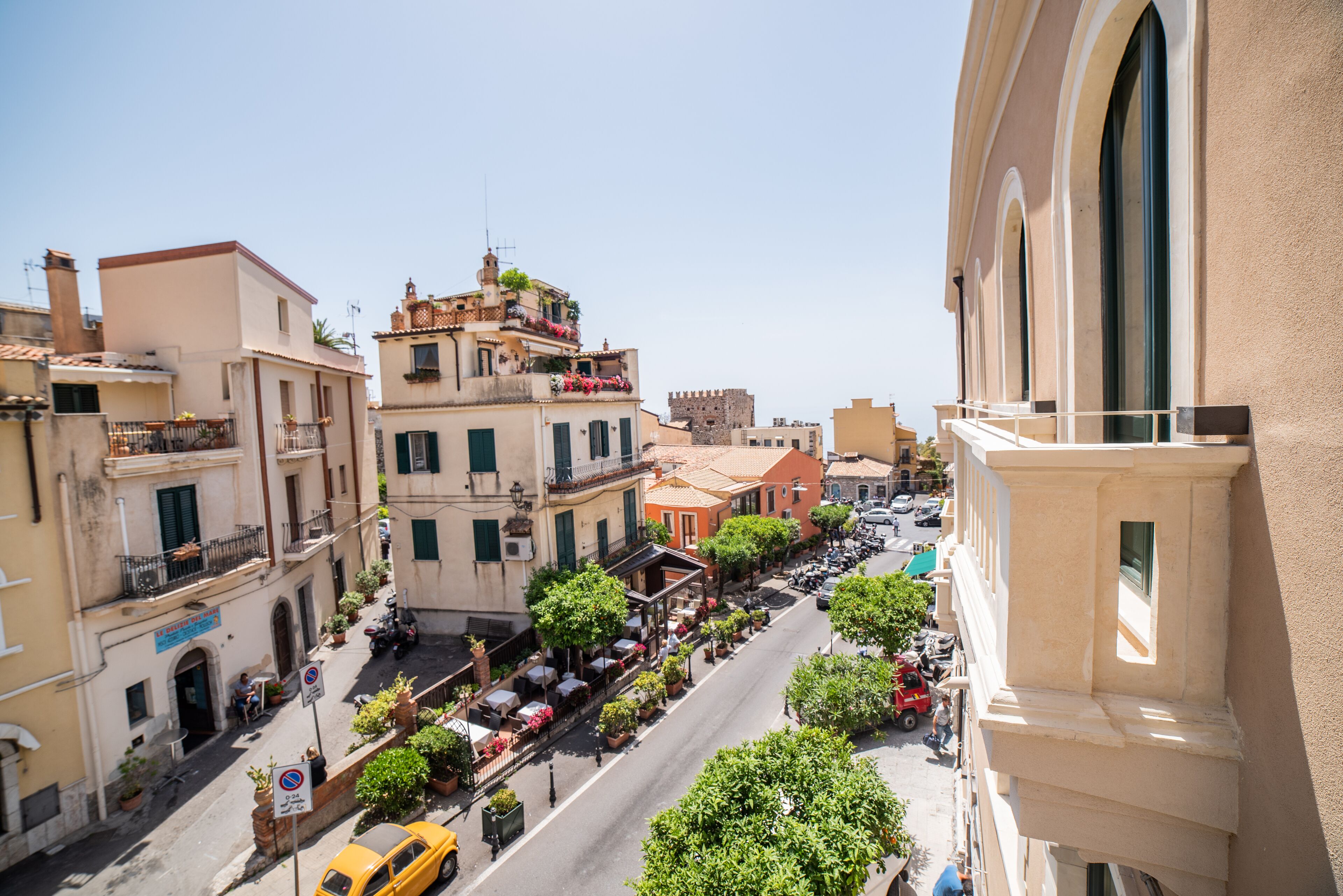 Una vista di strada di una cittadina storica con edifici, un taxi giallo e tavolini all'aperto nei caffè.