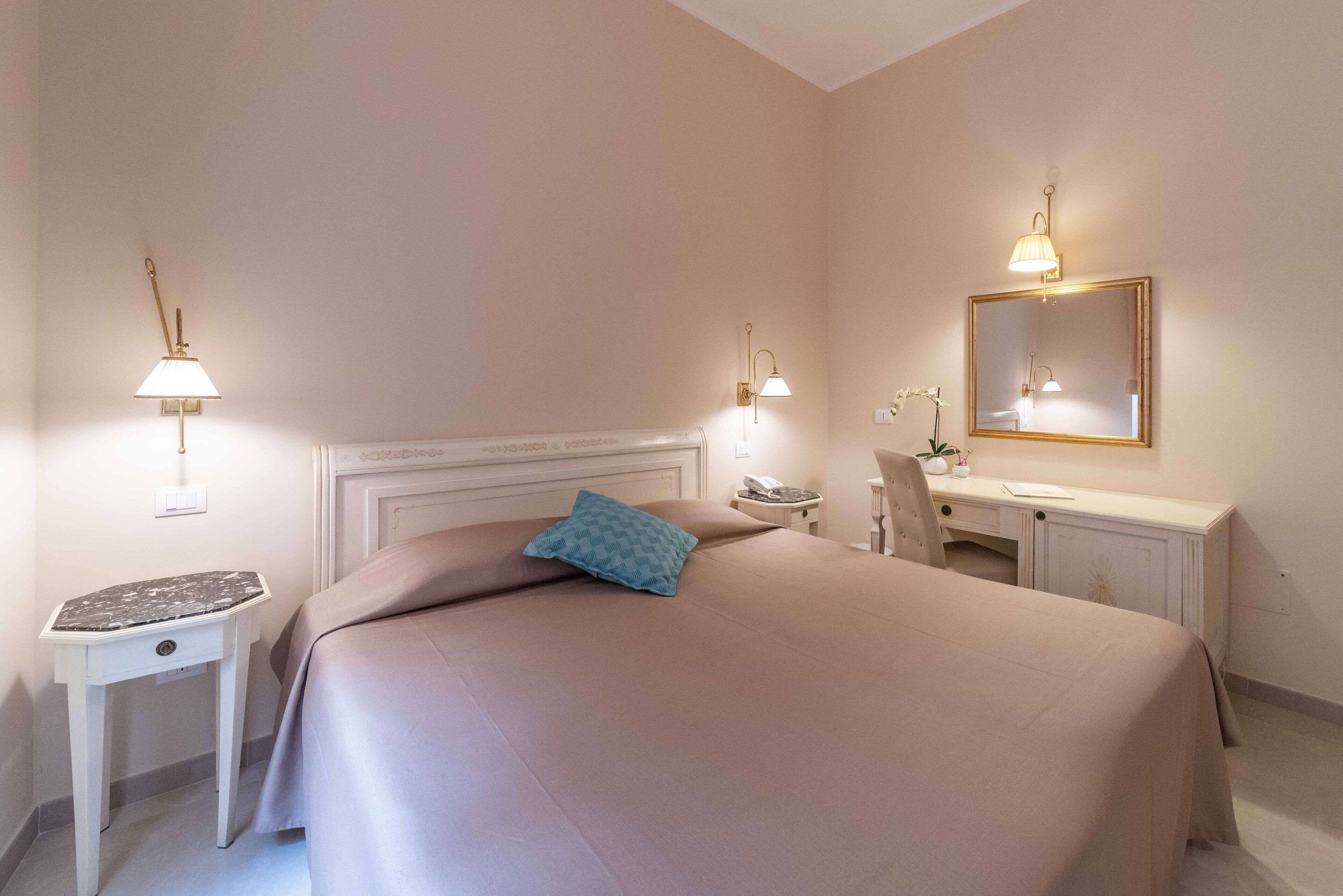 Un dormitorio ordenado con cama, mesitas de noche, un escritorio y un espejo.