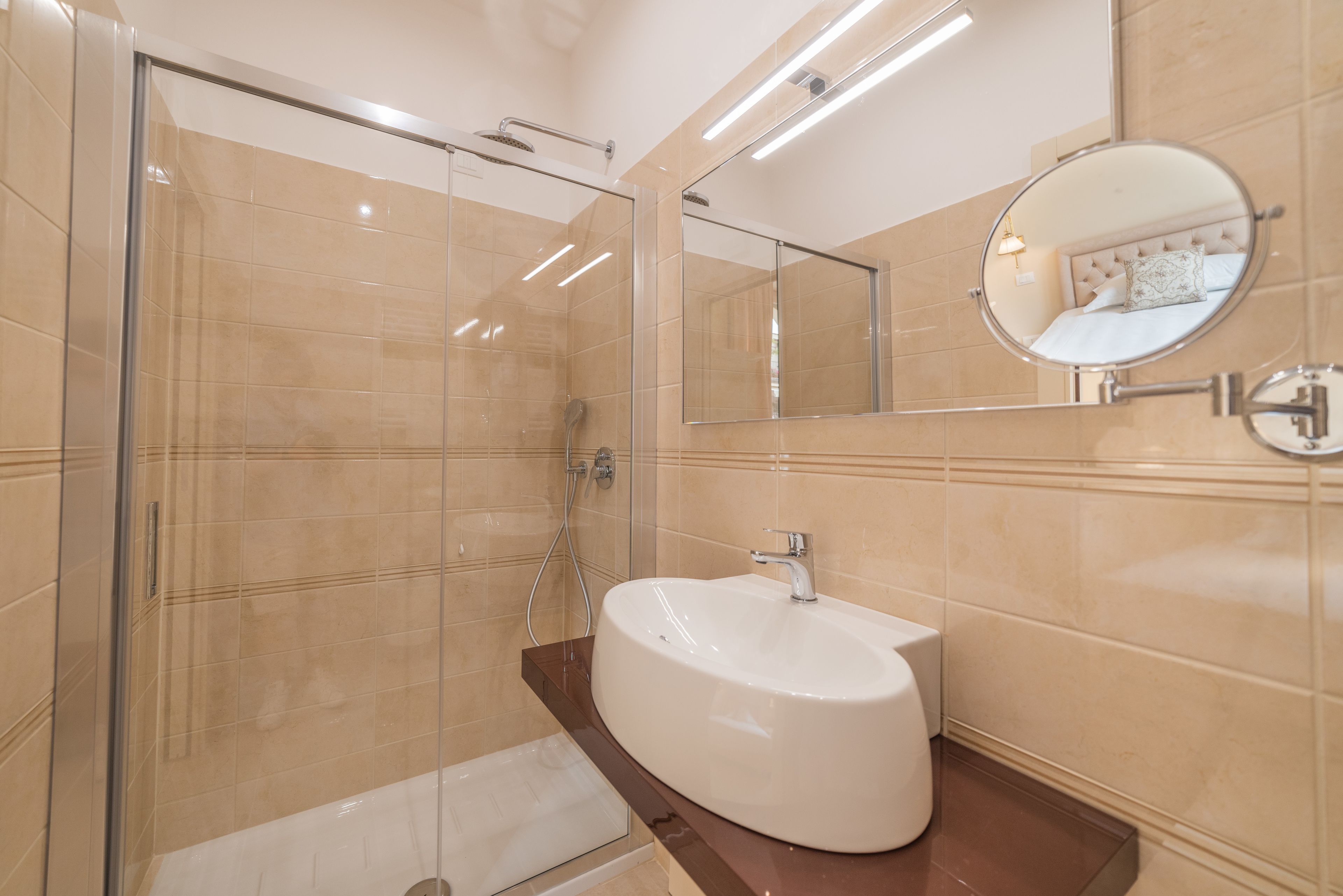 Un baño moderno con cabina de ducha de vidrio, un lavamanos blanco y un espejo con marco redondo.