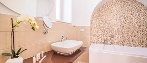 A modern bathroom with a large sink, a mirror, a bathtub, and a decorative wall.
