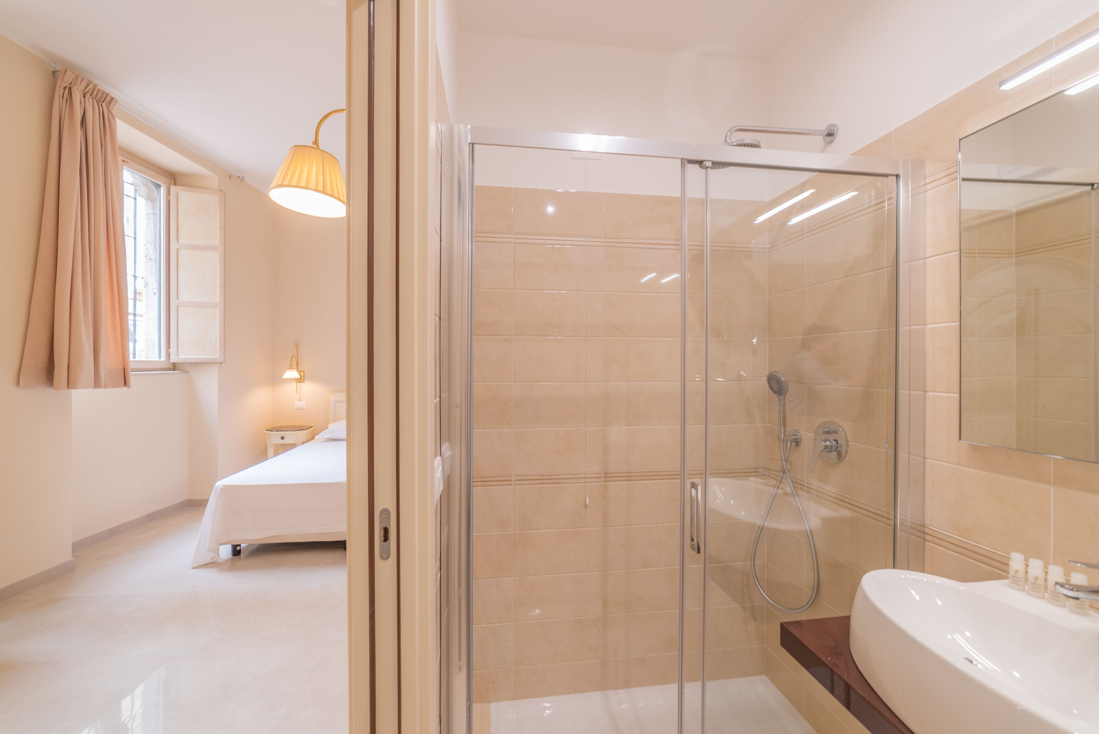 Un baño moderno con ducha envuelta en vidrio, una bañera grande y una mesita de noche con lámpara.