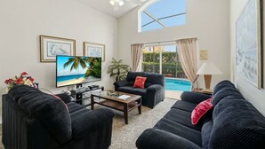 Ein Wohnzimmer mit Fernseher, schwarzen Sofas, einem Couchtisch, Deckenventilator und Blick auf einen Swimmingpool.