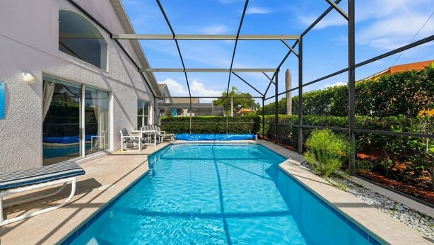 Ein Schwimmbecken mit überdachtem Bereich, eine Terrasse mit Stühlen und ein Blick auf ein Haus im Hintergrund.