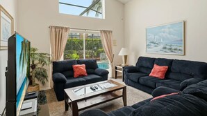 Ein geräumiges Wohnzimmer mit zwei schwarzen Sofas, einem Couchtisch, einem Fernseher und einem großen Fenster mit Vorhängen.