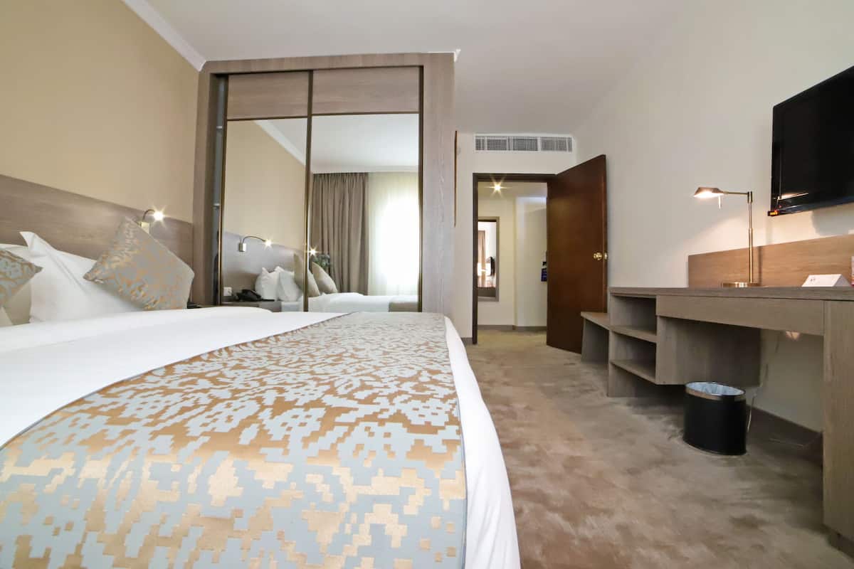 Ein Hotelzimmer mit einem großen Bett, einem Schreibtisch, einem Fernseher und einem Spiegel.