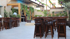 Un espace extérieur aménagé avec des tables et des chaises en bois, entouré de verdure et bordé d’un bâtiment dont le toit est recouvert de tuiles.