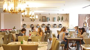 Un restaurant doté de plusieurs tables et chaises, d’un lustre et de luminaires fixés aux murs.