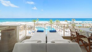 Un balcon avec deux chaises longues blanches, une piscine et une vue sur la plage et l’océan.