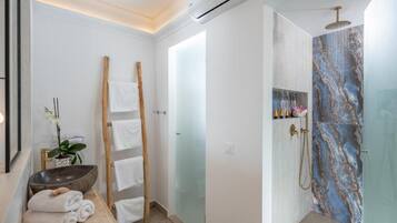 Un baño moderno con ducha de mármol, toallero de madera y un bol grande.