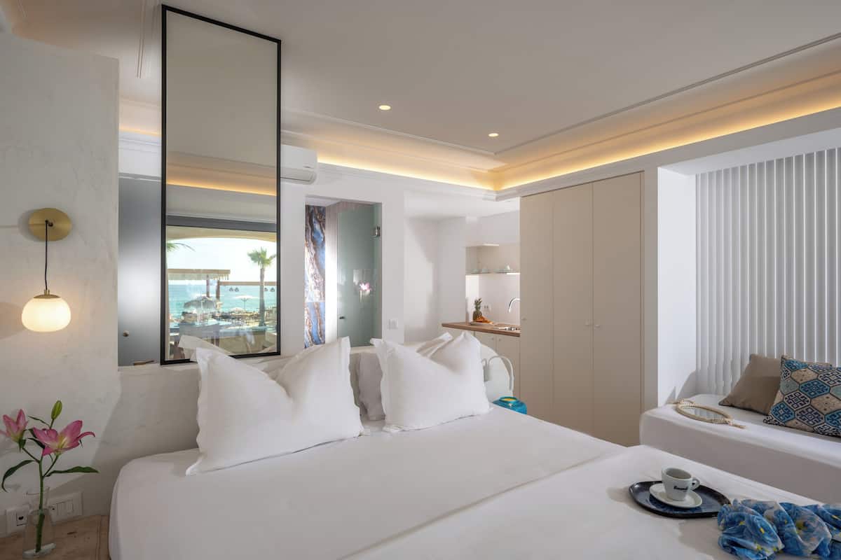 Habitación de hotel con cama, mesita de noche, lámpara y vistas a la zona de la piscina.