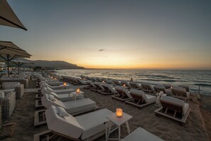 A beachside lounge area with sun loungers and tables, some with candles, overlooking the ocean. - Parthenis Beach Suites by the Sea (Hersonissos)
