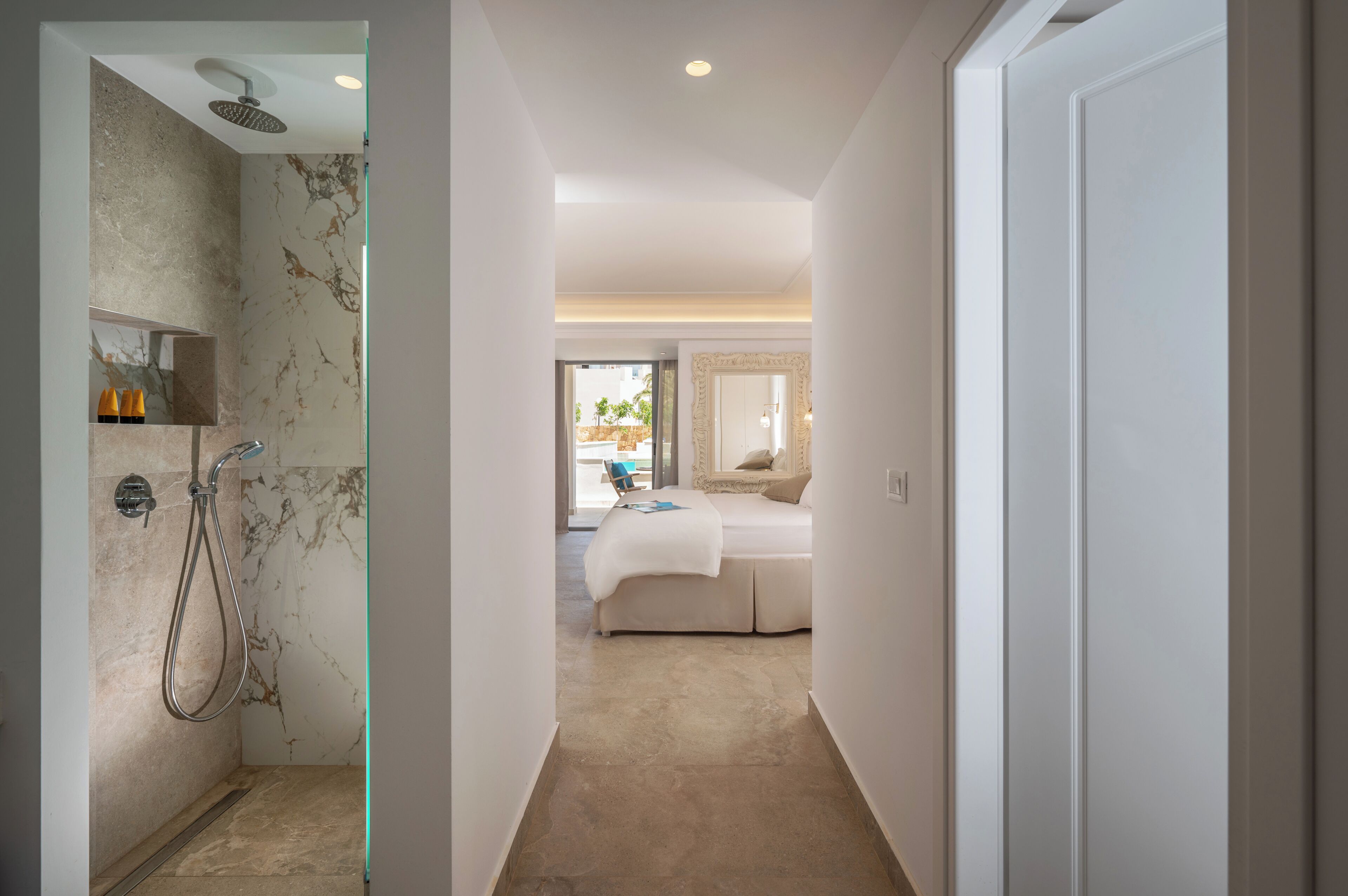 A hotel room with a shower, a bed, a bathroom mirror, and a view of the outdoors.