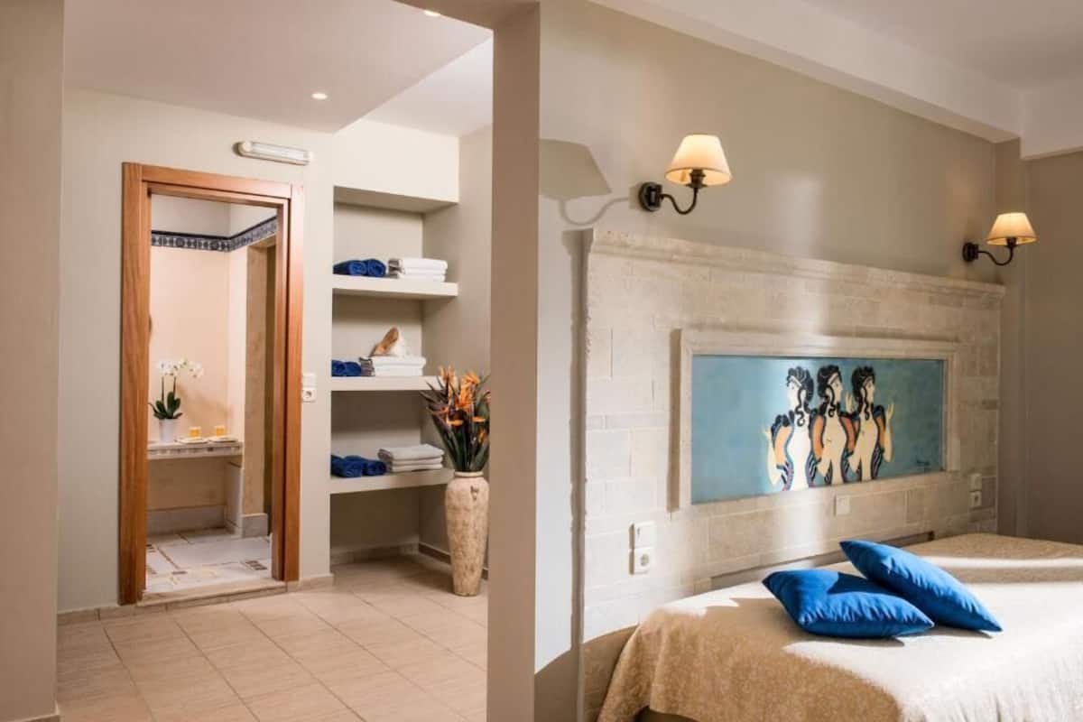 Una habitación de hotel con cama, un cuadro en la pared, chimenea y baño con ducha y estantes.