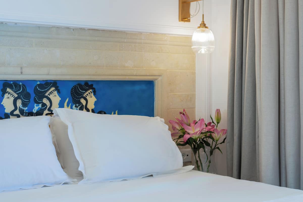 Habitación de hotel con una cama, una lámpara de pared, un cabecero decorativo y un jarrón con flores.