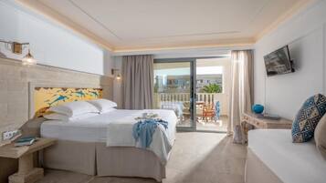 A hotel room with a bed, a sofa, a TV, a balcony with a table and chairs, and a view of buildings.