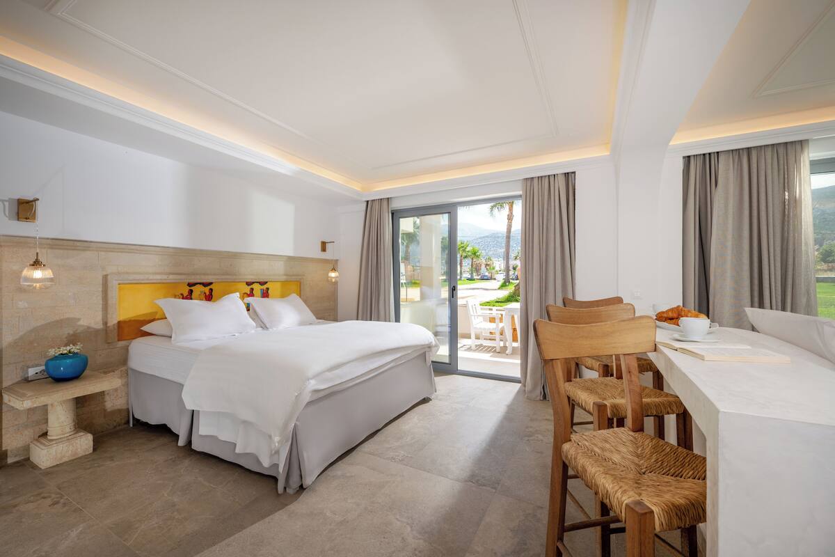 Habitación de hotel con cama, escritorio, sillas, una mesita y vistas al exterior.