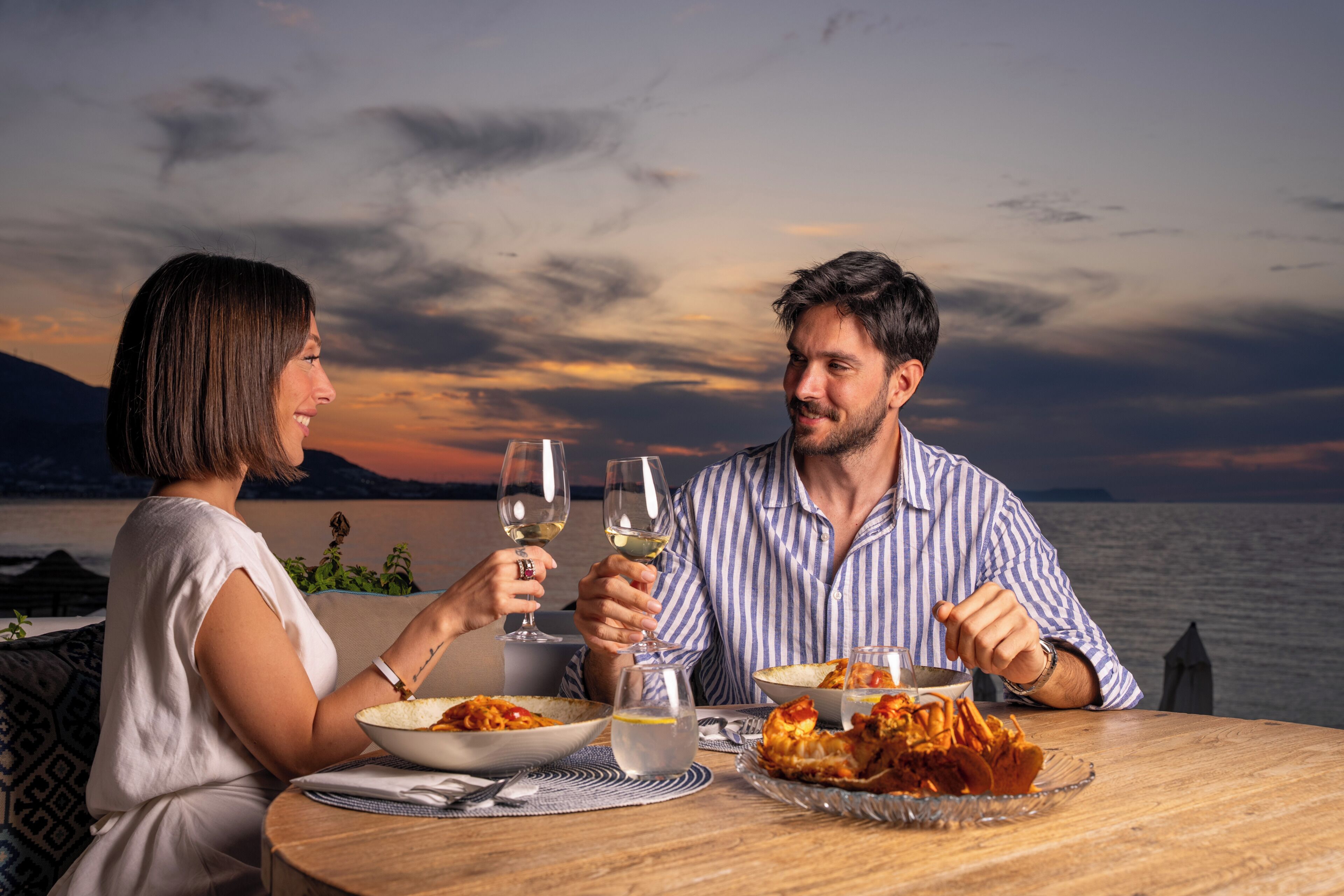 Una pareja cenando en una mesa con vista al mar y las montañas.