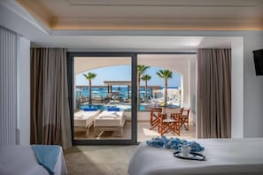 A hotel room with a bed, a view of a pool area, and a dining table with chairs. - Parthenis Beach Suites by the Sea (Hersonissos)