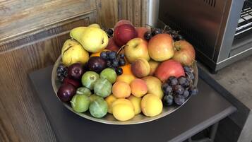 A fruit bowl on a table next to a wooden door and a bread box.