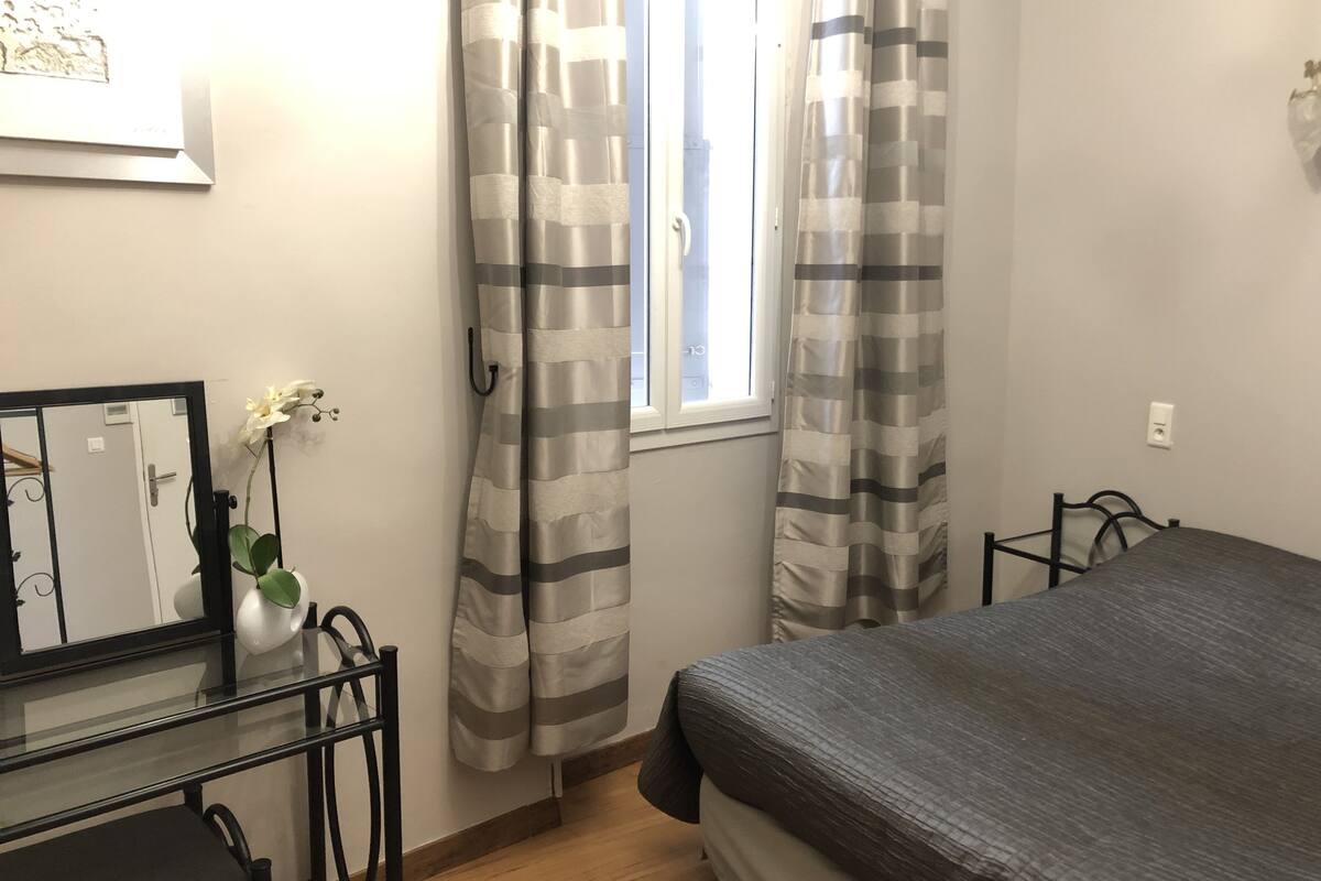Ein Schlafzimmer mit Bett, Kommode, Spiegel und einem Fenster mit Vorhängen.