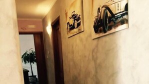 A hallway with a beige couch, a patterned rug, and two wall-mounted car paintings. - B&B Lolly (Mileto)