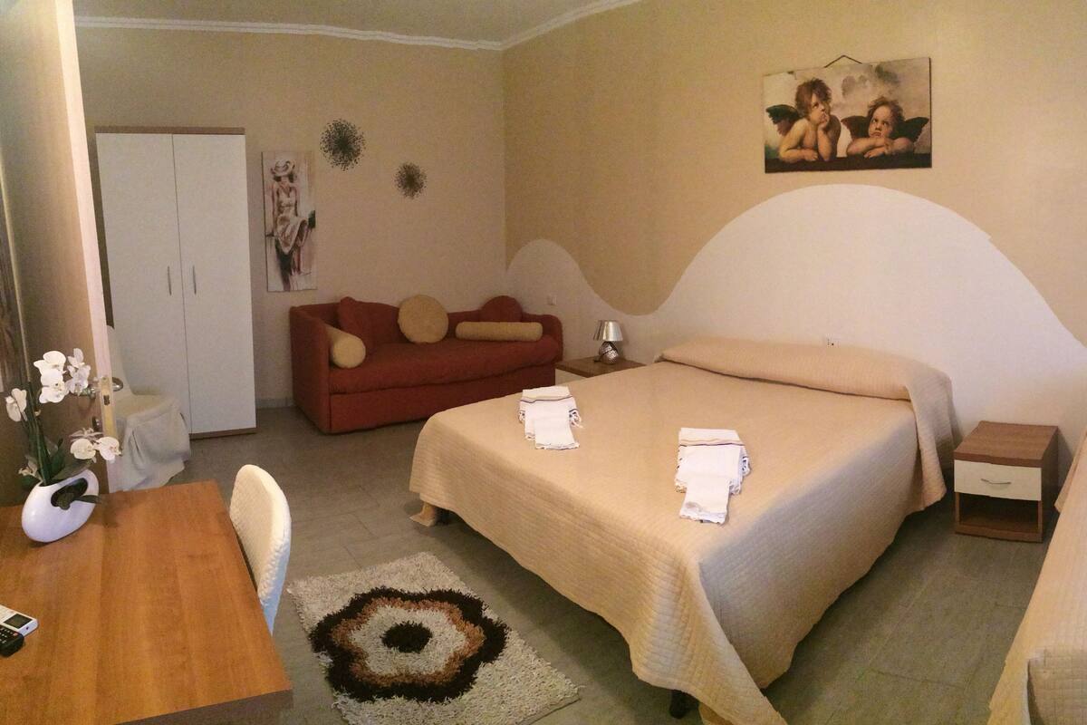 Habitación de hotel con dos camas, un sofá, una mesita y un tapete decorativo.