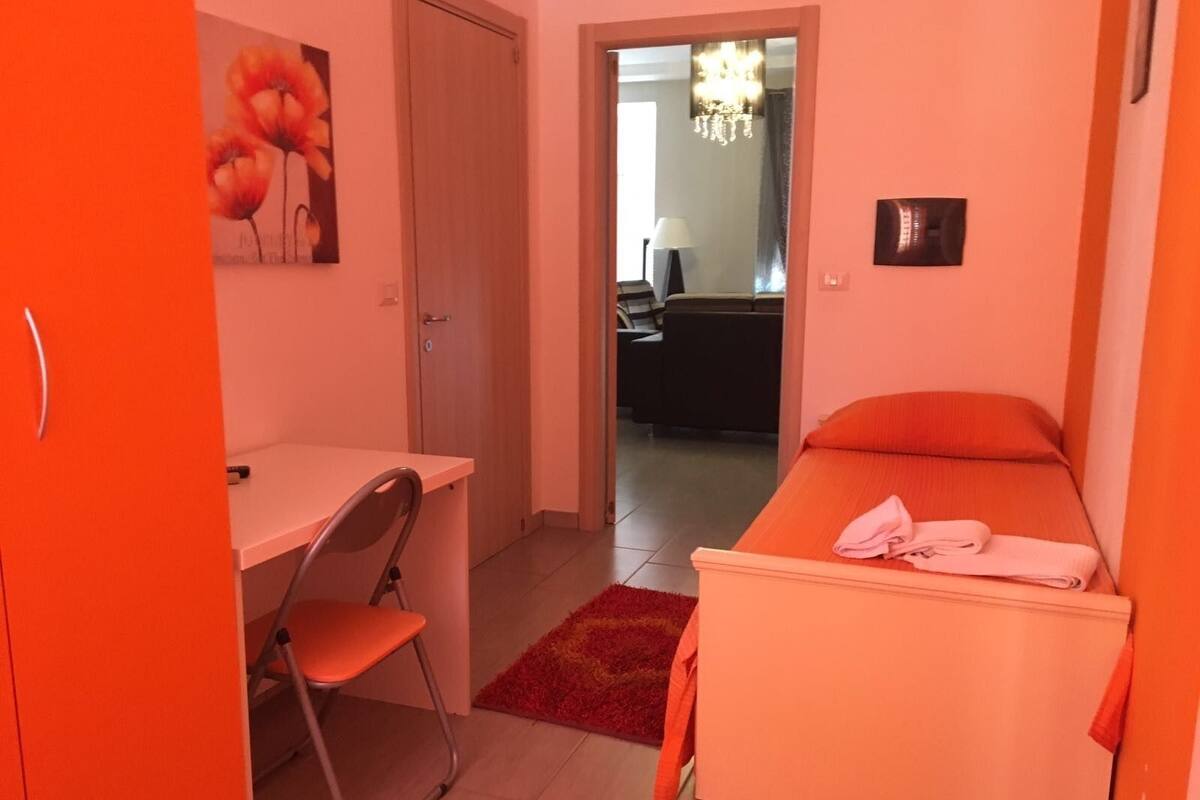 Una habitación pequeña con decoración naranja, una cama, una silla y un escritorio.