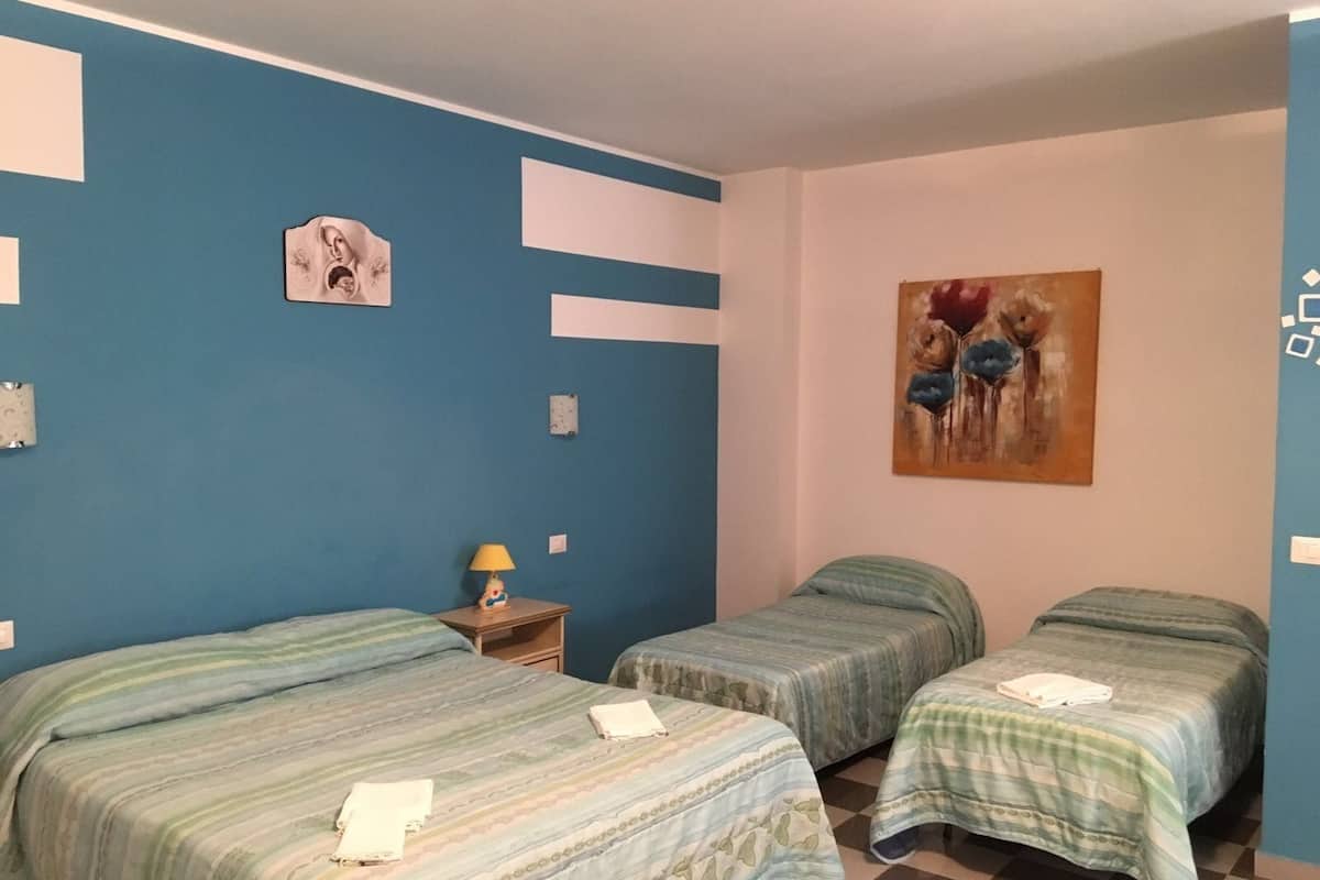 Una habitación con dos camas, una mesita de noche con una lámpara y un cuadro en la pared.