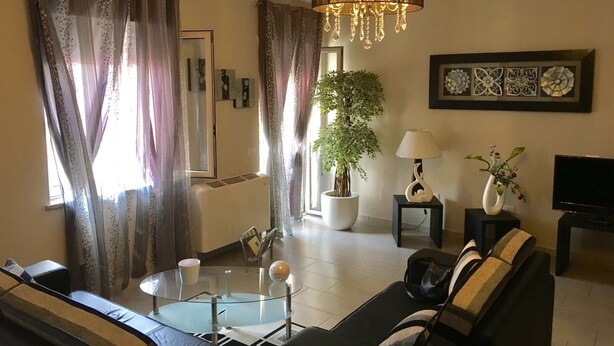 A living room with a black sofa, a glass coffee table, a potted plant, a chandelier, and artwork on the walls. - B&B Lolly (Mileto)