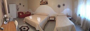 A hotel room with two beds, a red sofa, a wooden table, and a small bedside table with a lamp. - B&B Lolly (Mileto)