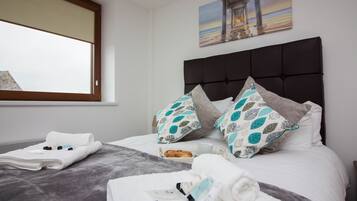 Una cama bien hecha con una manta gris, toallas blancas y una bandeja de desayuno con croissants.