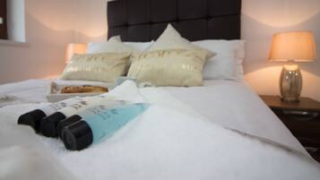 Un letto rifatto con lenzuola bianche, una testiera nera e cuscini decorativi con scritte. Sul letto ci sono due flaconi di lozione.