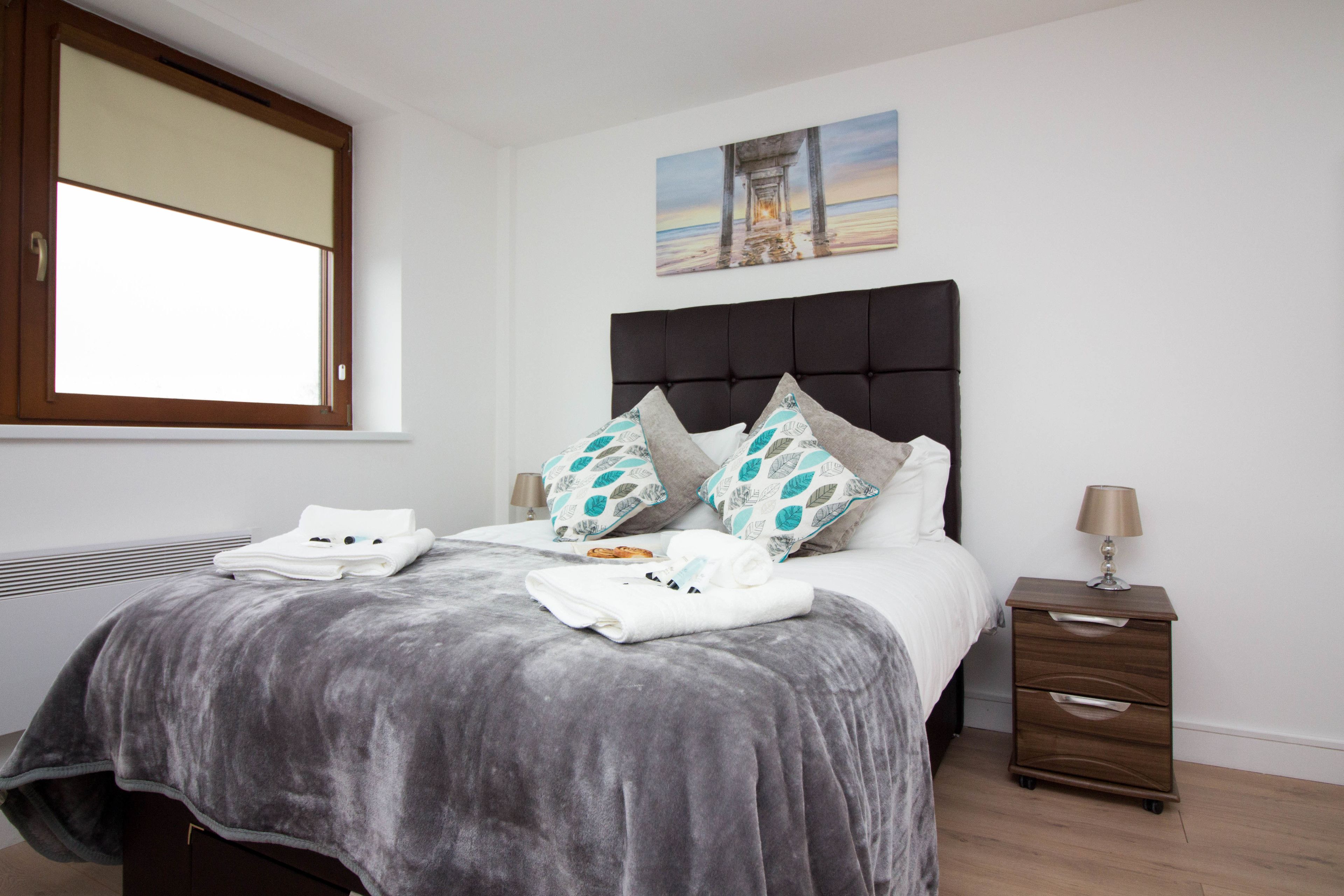 A bedroom with a large bed, a nightstand, a lamp, and a window.