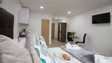Una habitación de hotel moderna con una cama, un televisor de pantalla plana, una mesita con un florero y una silla.