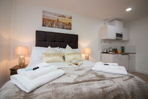 A hotel room with a bed, two bedside lamps, a cityscape painting, a microwave, and a small kitchenette. - Trafalgar House (Stoke-on-Trent)