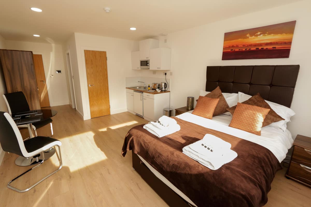 Habitación de hotel con cama, escritorio, silla, kitchenette y un cuadro en la pared.