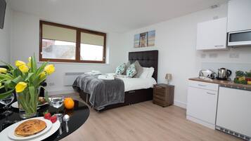 Ein modernes Hotelzimmer mit Bett, Nachttisch und einer kleinen Küchenzeile.
