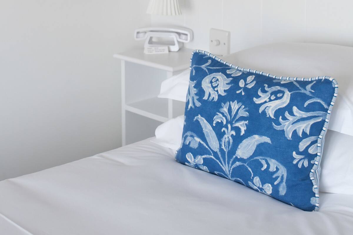 A neatly arranged bedroom with a bed, a bedside table with a lamp, and a window with frosted glass panels.